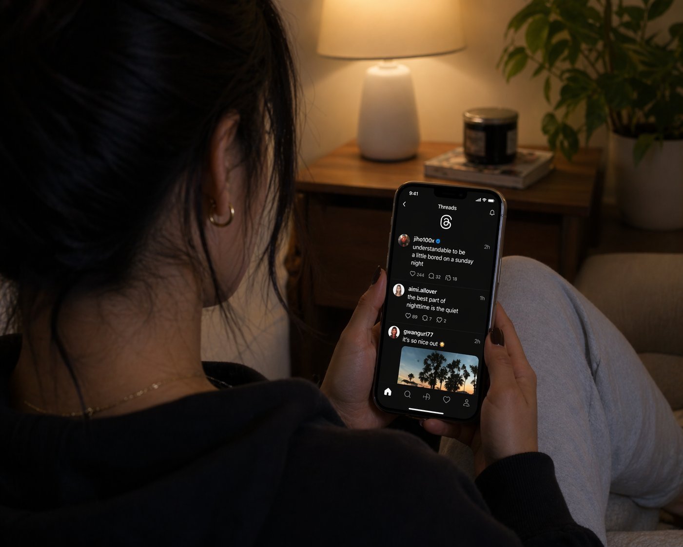 A woman scrolling the Threads feed on her phone in a cozy evening setting